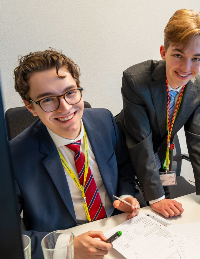 Drei Teilnehmende am Schreibtisch lachen in die Kamera
